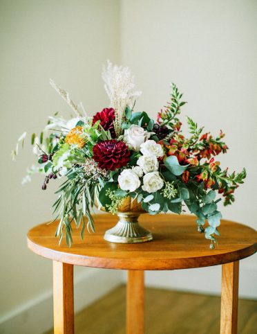 Vibrant wedding flower centerpiece on circular wooden table with white background