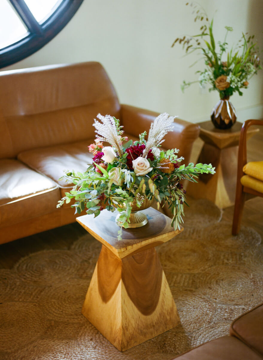 Wedding floral arrangement on wooden stand in room with couches and chair