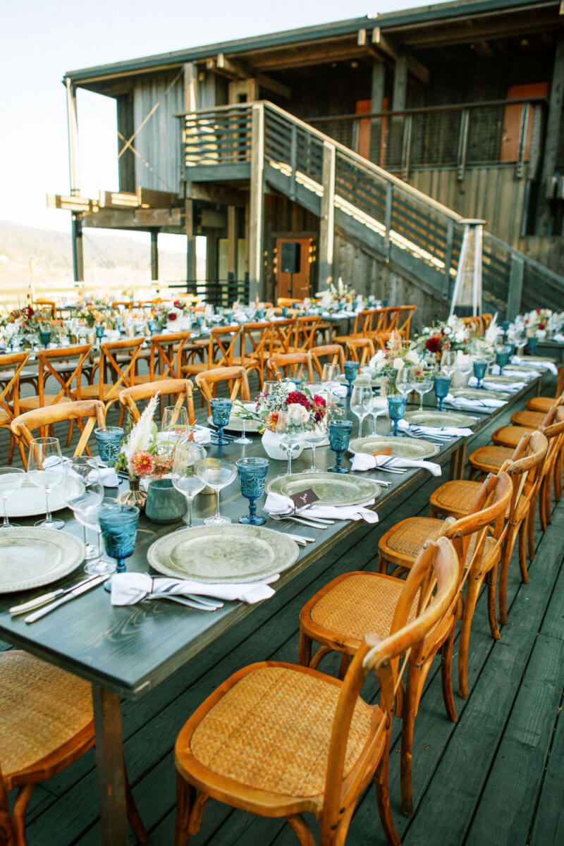 Wedding reception table fully set and decorated with floral arrangements on outdoor deck