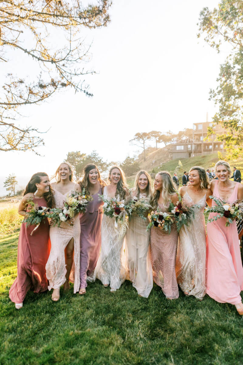 Group of 7 bridesmaids and bride holding wedding bouquets with Sonoma County outdoors and groomsmen in background