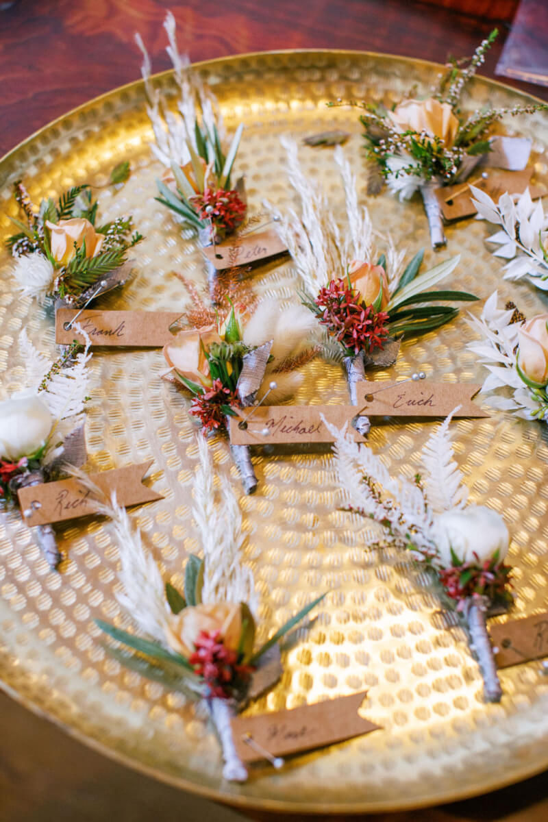 Floral wedding corsages for groomsmen, labeled on golden serving platter