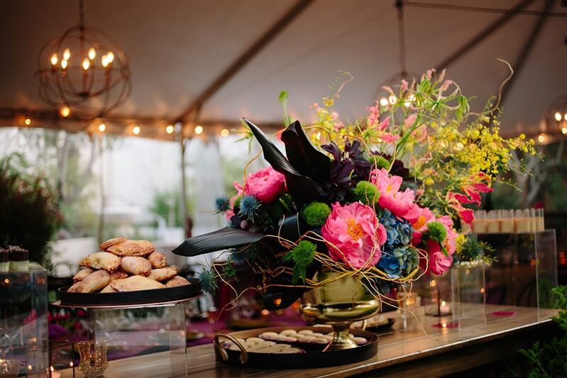 Rustic flower arrangement set atop wooden table to miniature pastries