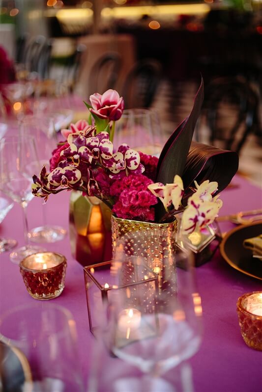 Pink birthday event floral centerpieces on dining table next to candles and glasses
