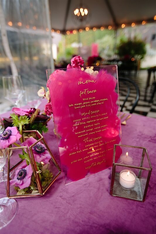 Vibrant pink floral arrangements set on table next to candles and birthday event menu