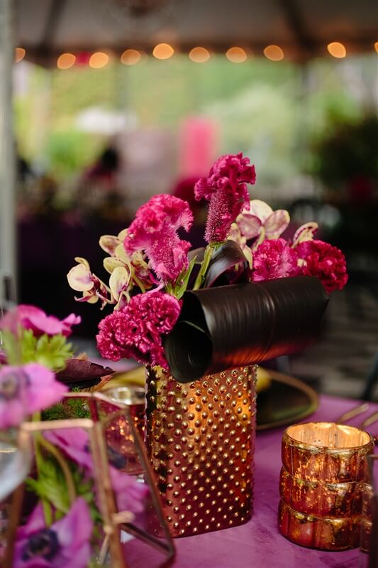 Birthday event floral arrangement in brass container set next to a brass mug on a table with pink tabecloth