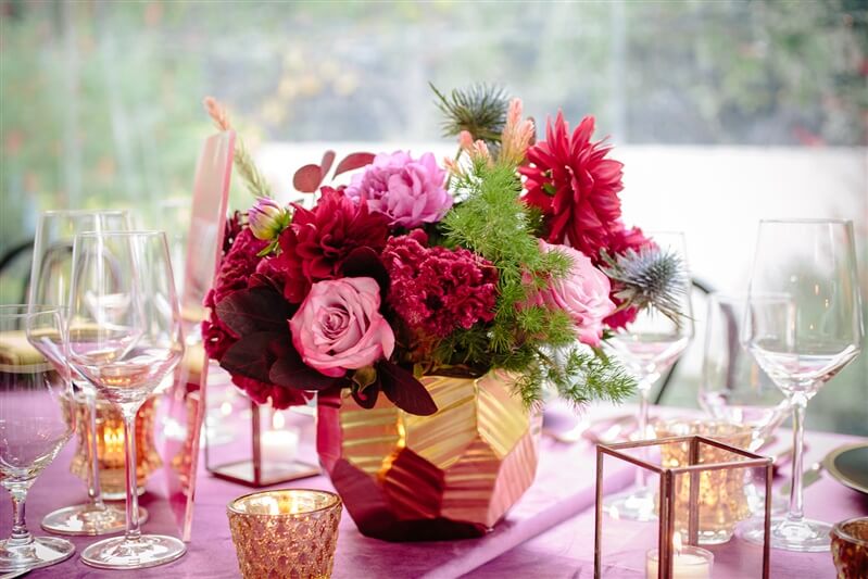 A pink floral arrangement on set dinner table with pink tablecloth and candles
