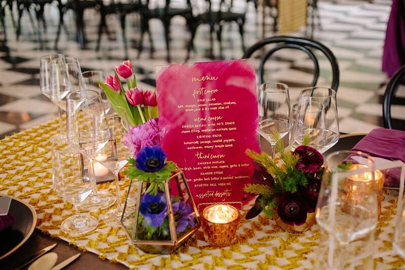 Fully set birthday party table with small flower arrangements and a pink dinner menu