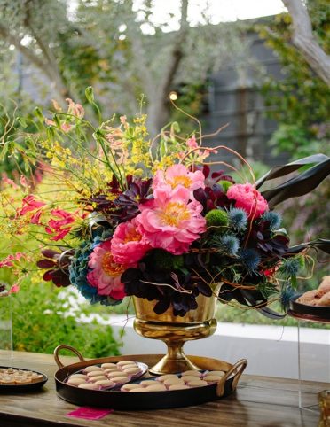 A multicolored floral arrangement on table outside set next to miniature pastries at birthday event