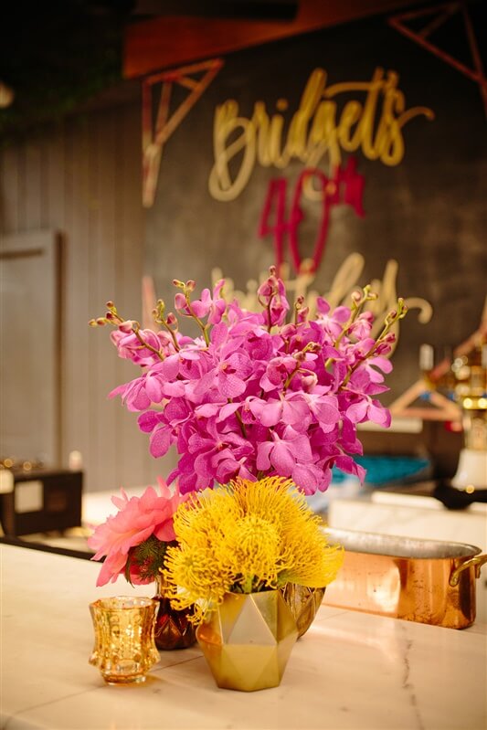 Pink and yellow birthday event flower arrangements set up on outdoor dining table