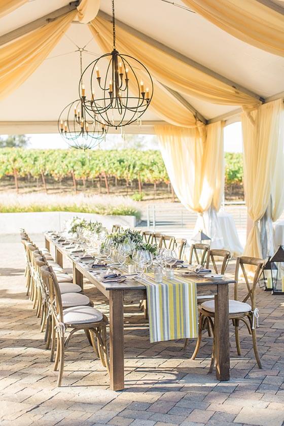 Outdoor Williams Seylem Winery dining table set with floral arrangements under tent and chandeliers; floral design by Healdsburg florist Aimee Lomeli Designs
