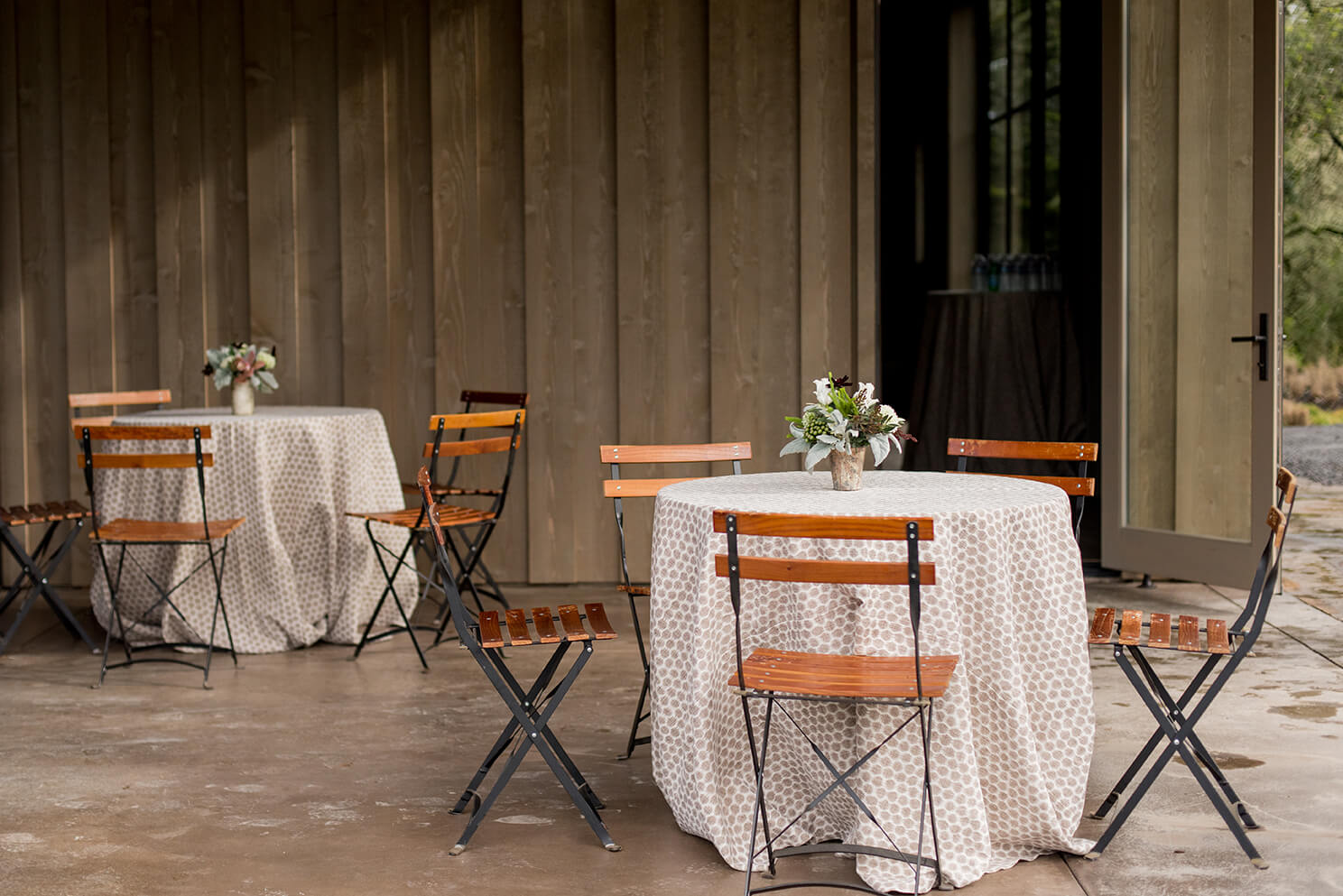 Two round tables with rustic floral centerpieces in front of wooden building at Sonoma county winery