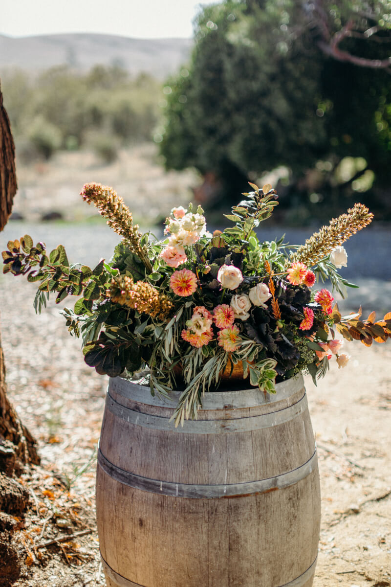 Rustic floral wedding arrangement set atop wine barrel outdoors at Stemple Creek Ranch