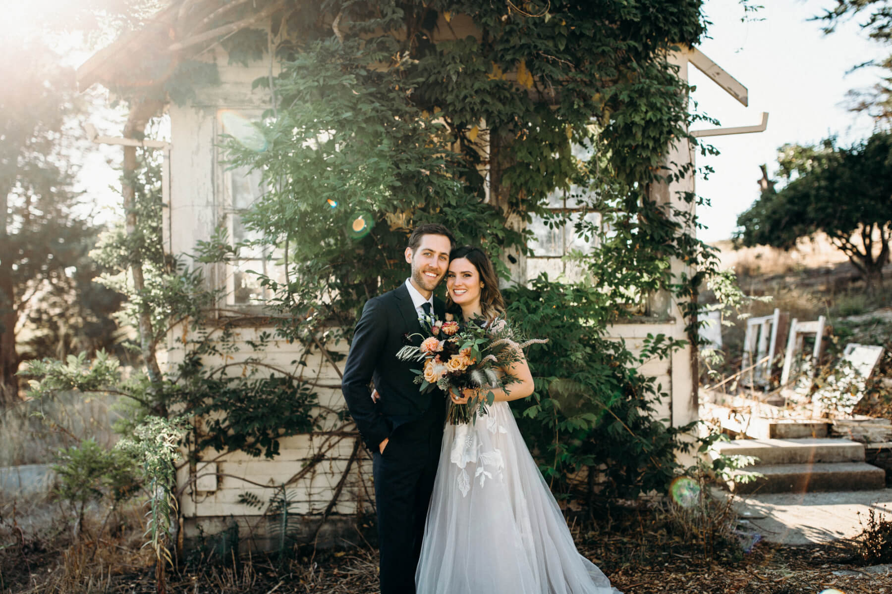 Groom and bride holding floral wedding bouquet standing in front of rustic ranch building outdoors at Stemple Creek Ranch in Marin County