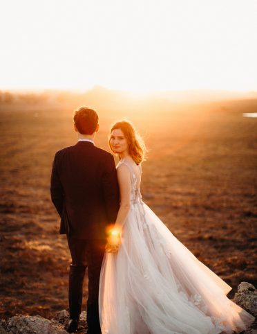 Bride and groom holding hands with backs to camera and bride looking back under Marin county sunset