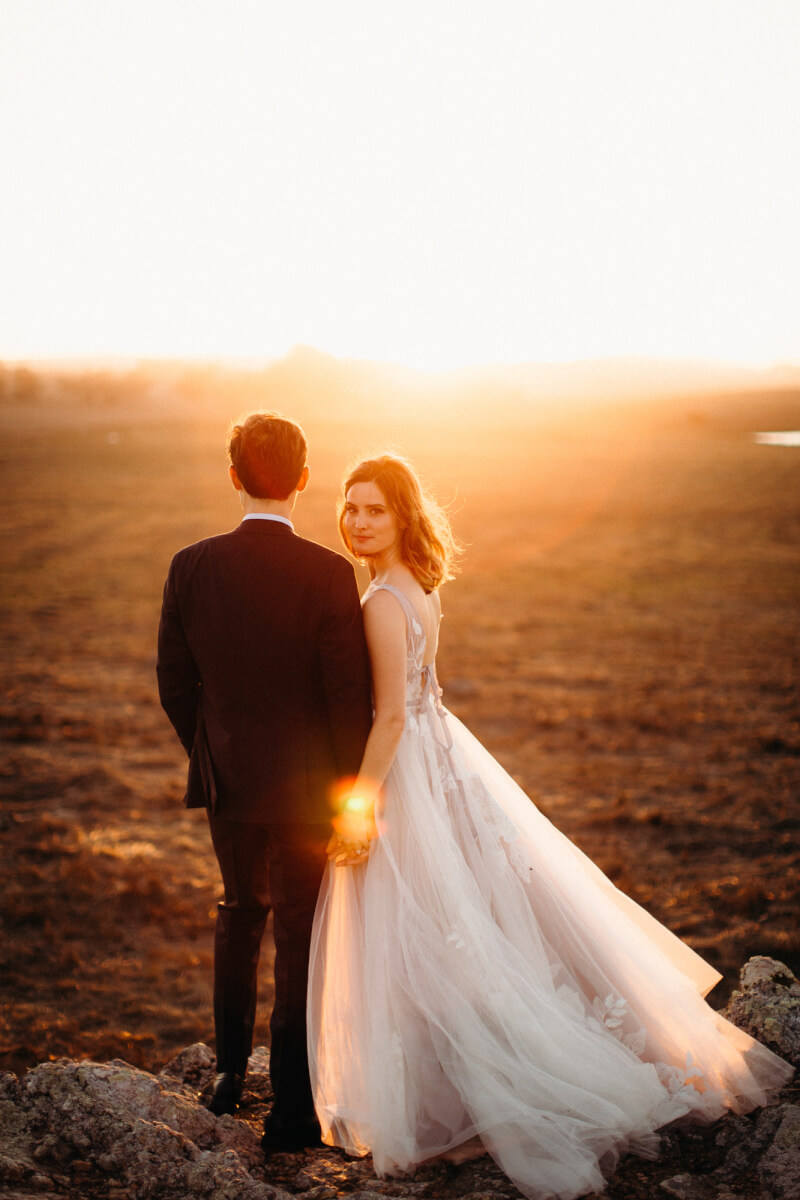 Bride and groom holding hands with backs to camera and bride looking back under Marin county sunset