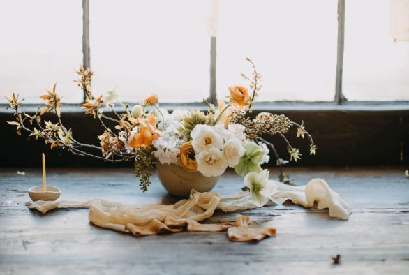 Rustic white and peach colored flower arrangement on wooden table with candle