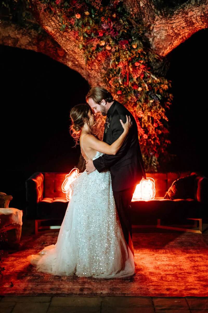 a bride and groom dancing at night under a tree decorated with flowers