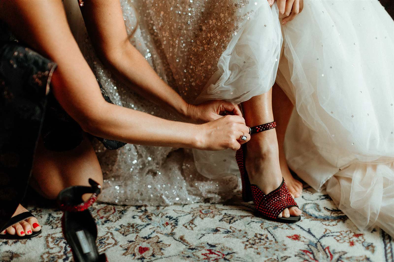 close up of bridesmaid helping bride put on red sparkly shoes