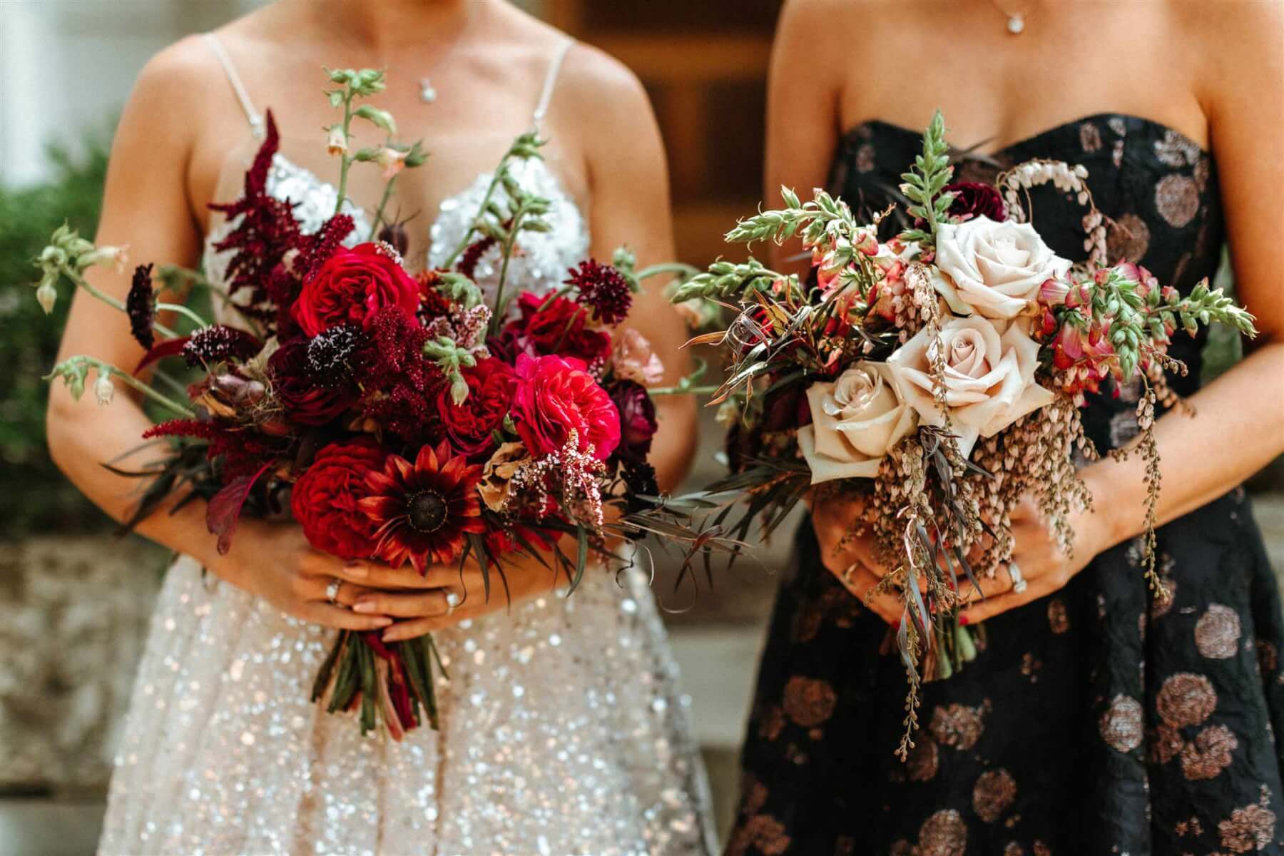 close up of a bride in white holding red flowers and a bridesmaid in a black dress holding pale pink flowers