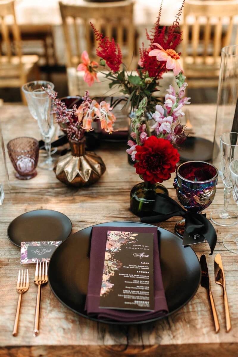 an outdoor wedding place setting with menu, plate, and flowers in various size vases