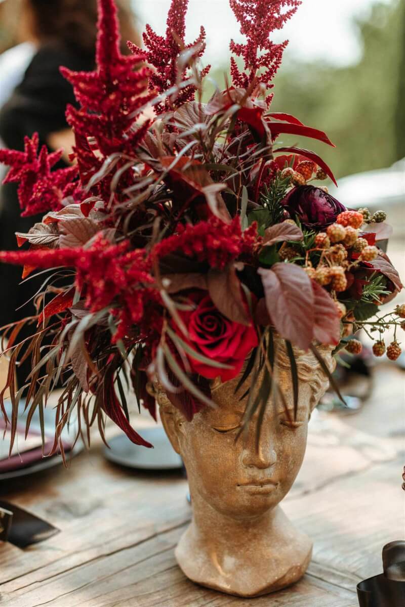close up of a red floral arrangement in a small stone vase shaped like a greek headpiece figurine