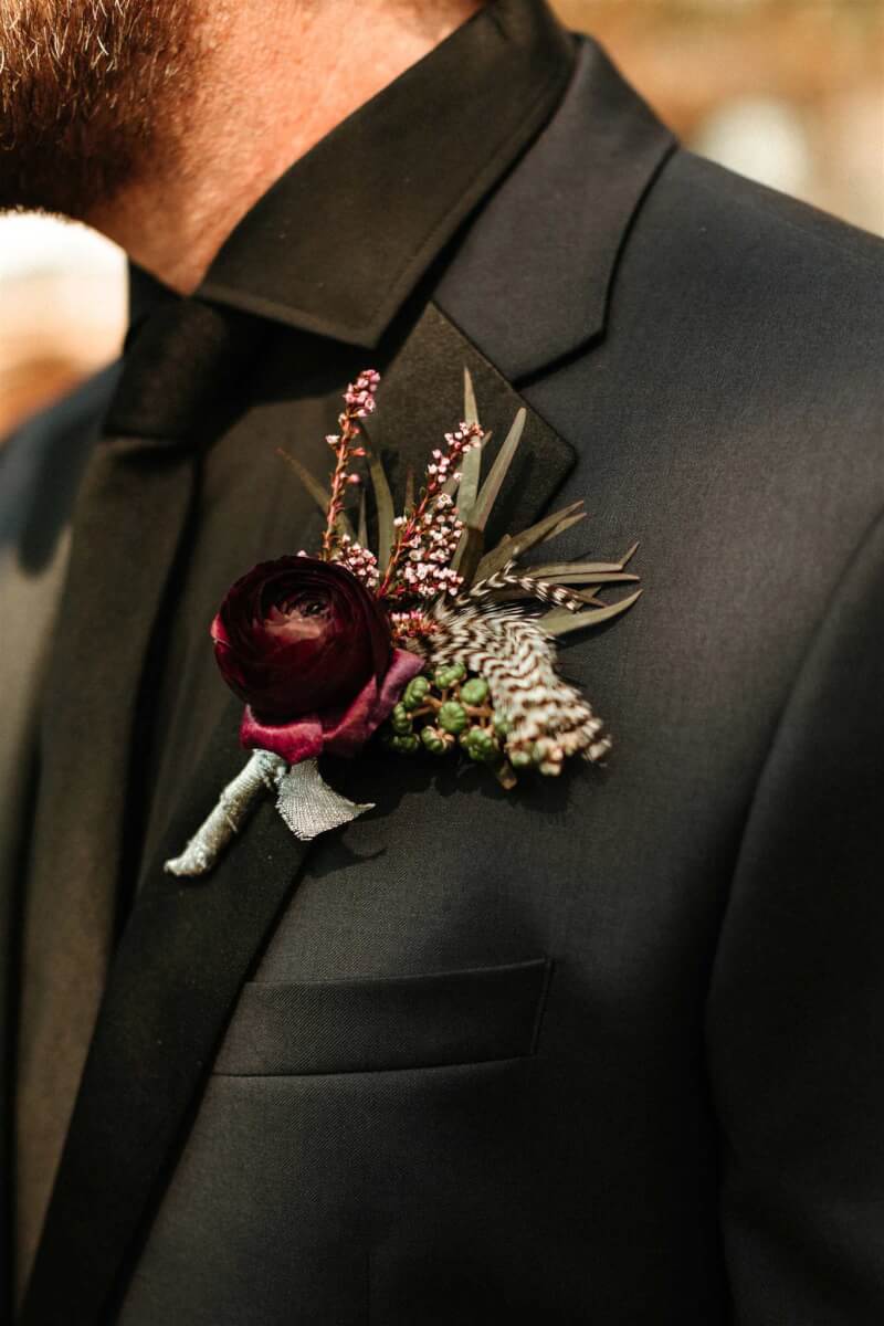close up of a wedding boutonniere on the lapel of a black suit with black shirt and tie