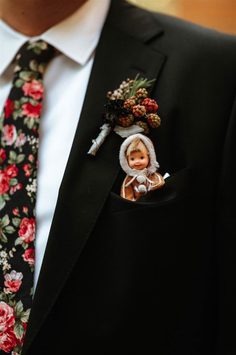 close up of a men's wedding lapel with a floral tie, flower decoration, and small doll in the pocket