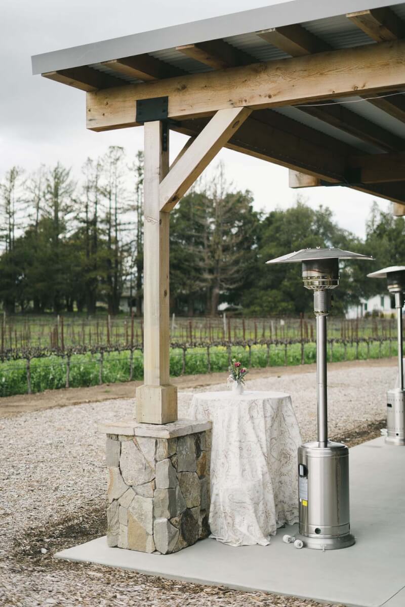 An outdoor space at a winery with unlit heat lamps and tall tables with flower arrangements