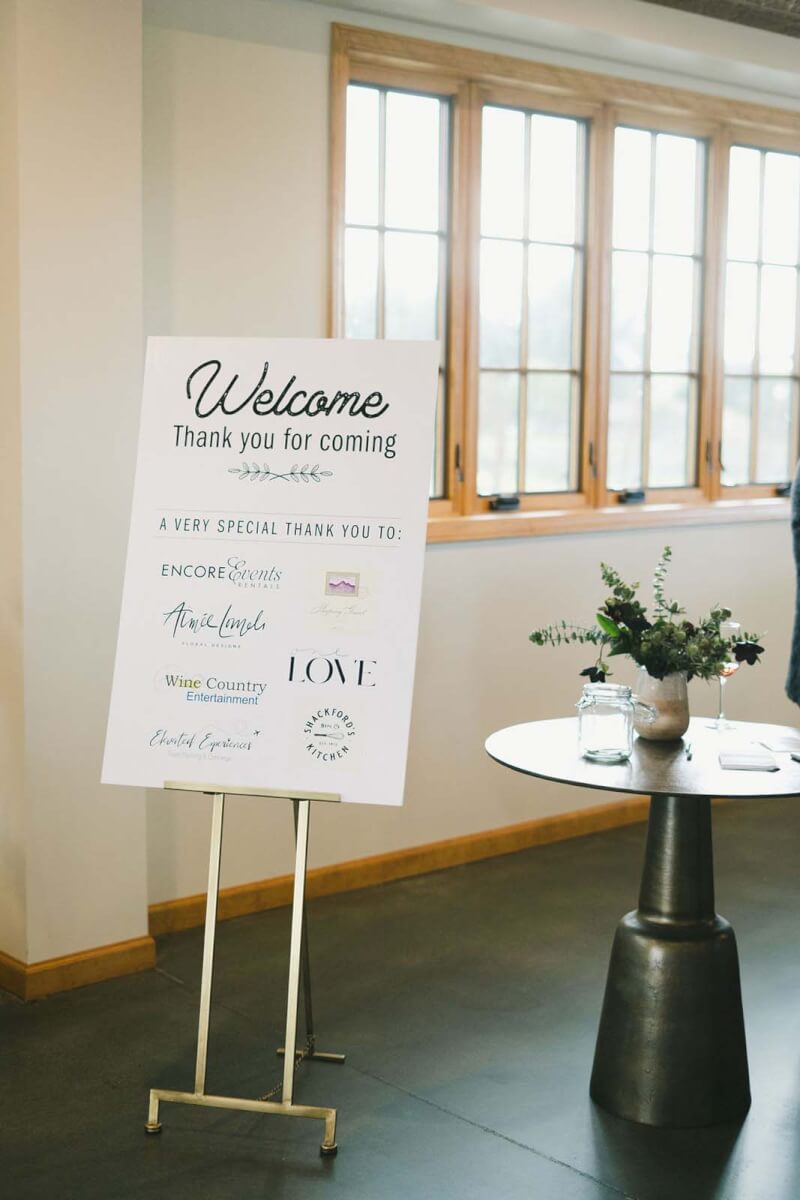 A welcome sign at a winery corporate event with elegant flowers on the table next to it