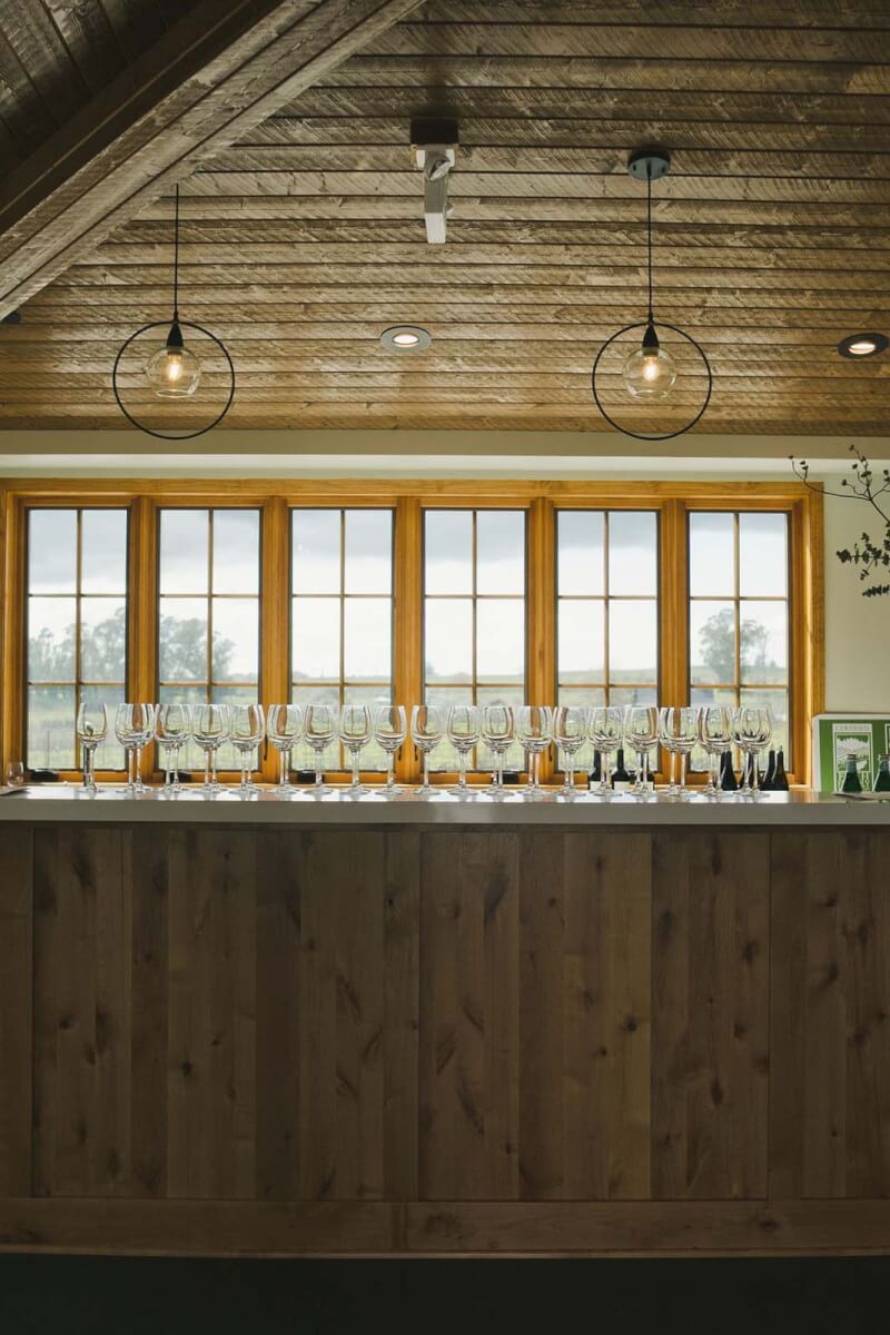 a view of a winery counter with high ceilings, modern chandeliers, and wine glasses lined up