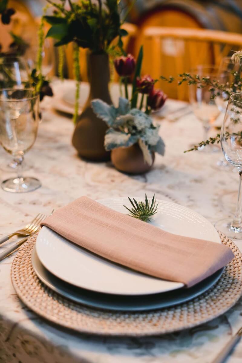 a place setting with a woven charger, beige napkin, and flowers all around