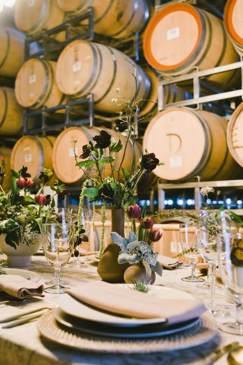corporate account winery flowers by aimee lomeli on a set table with wine barrels in the background