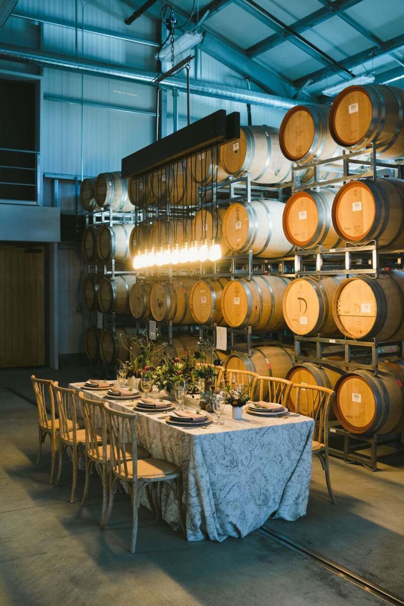 a table is set with flowers next to a rack of wine barrels