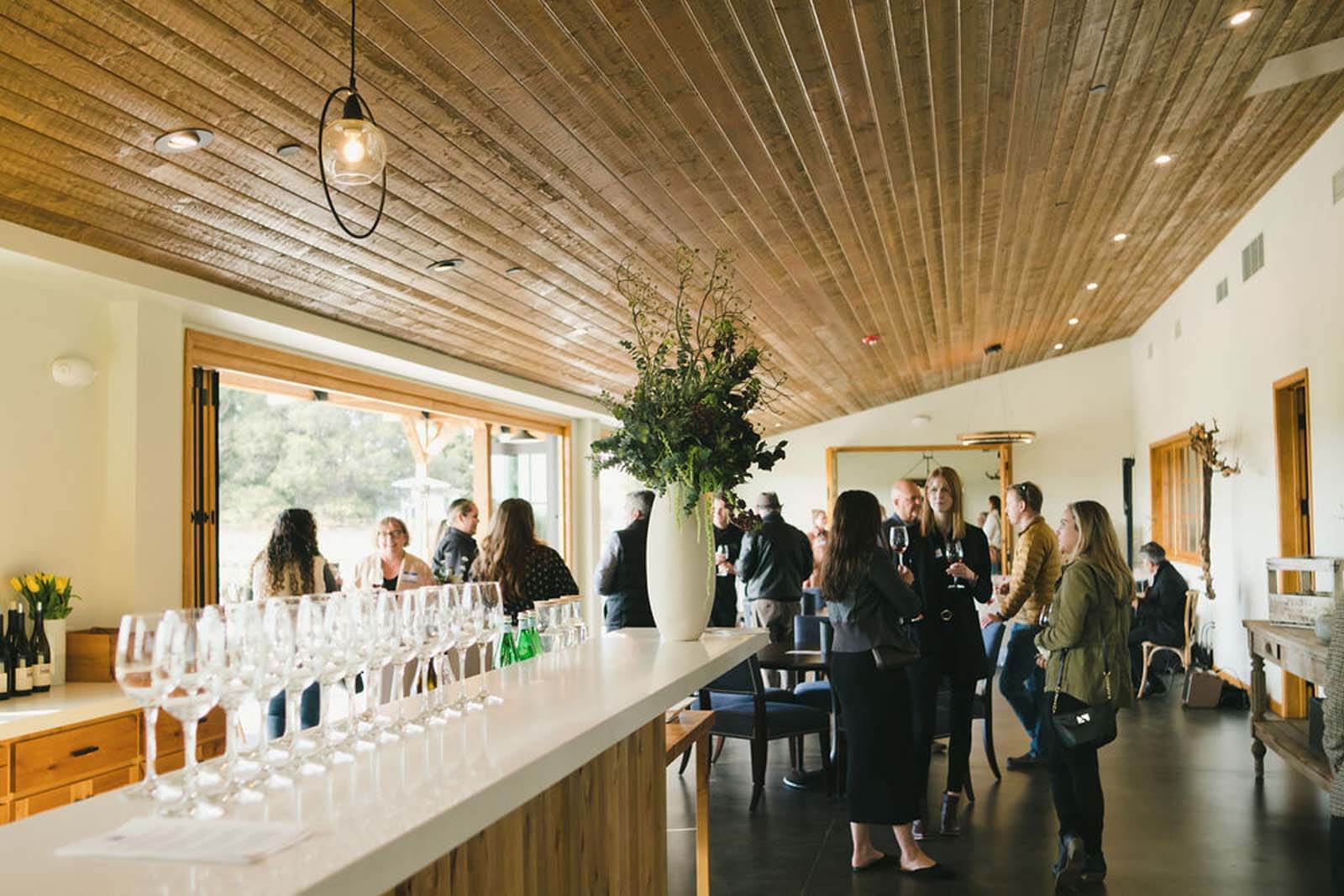 a corporate wine event with people standing around a bar filled with wine glasses and a floral arrangement
