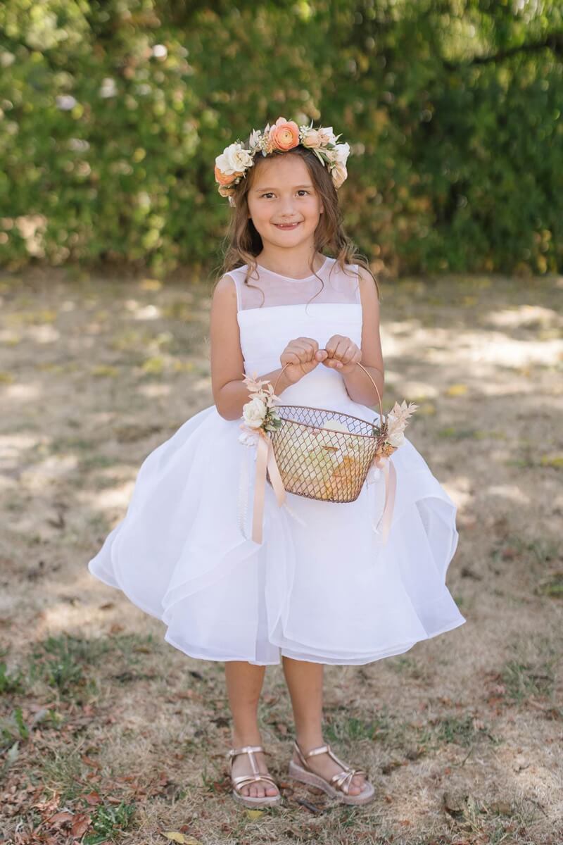 the flower girl in a white dress, wearing a floral crown, holding a basket filled with rose petals