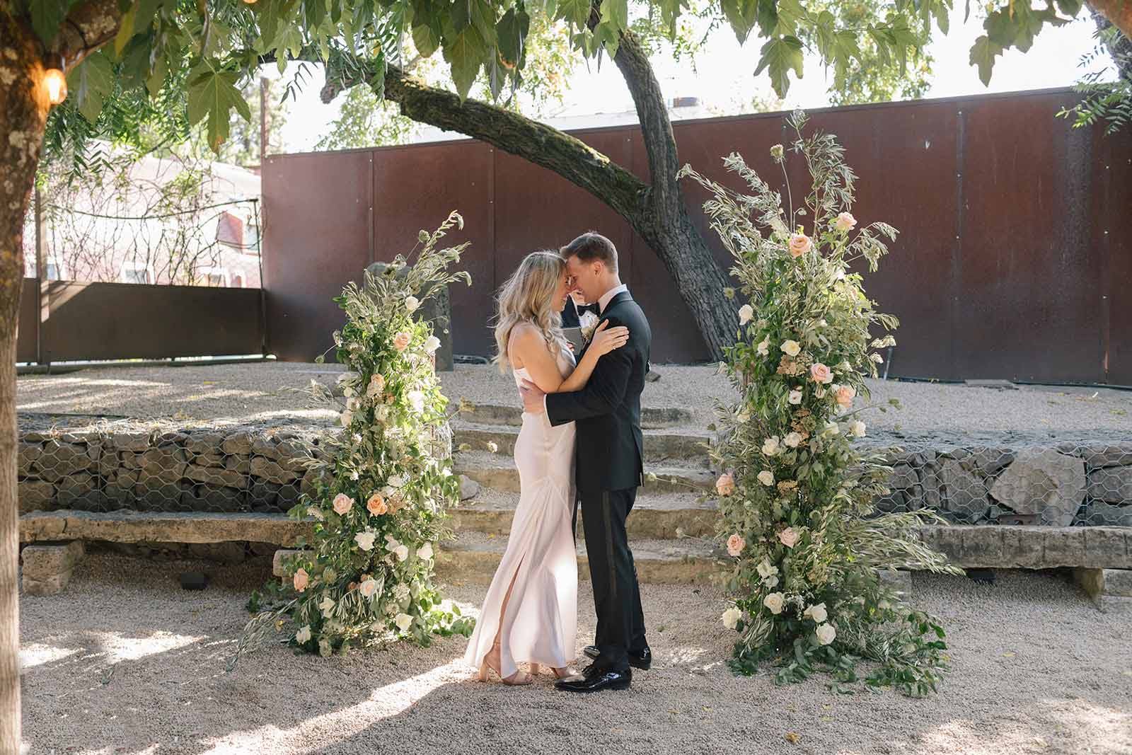 the bride and groom touching foreheads at a natural wild flower outdoor altar