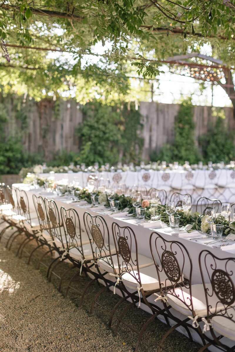 a long table set up for an outdoor wedding reception with elegant flowers and greenery