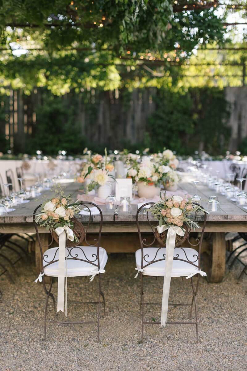 the bride and groom's chairs, decorated with flowers and ribbon, at the head of a large elegantly set wooden table