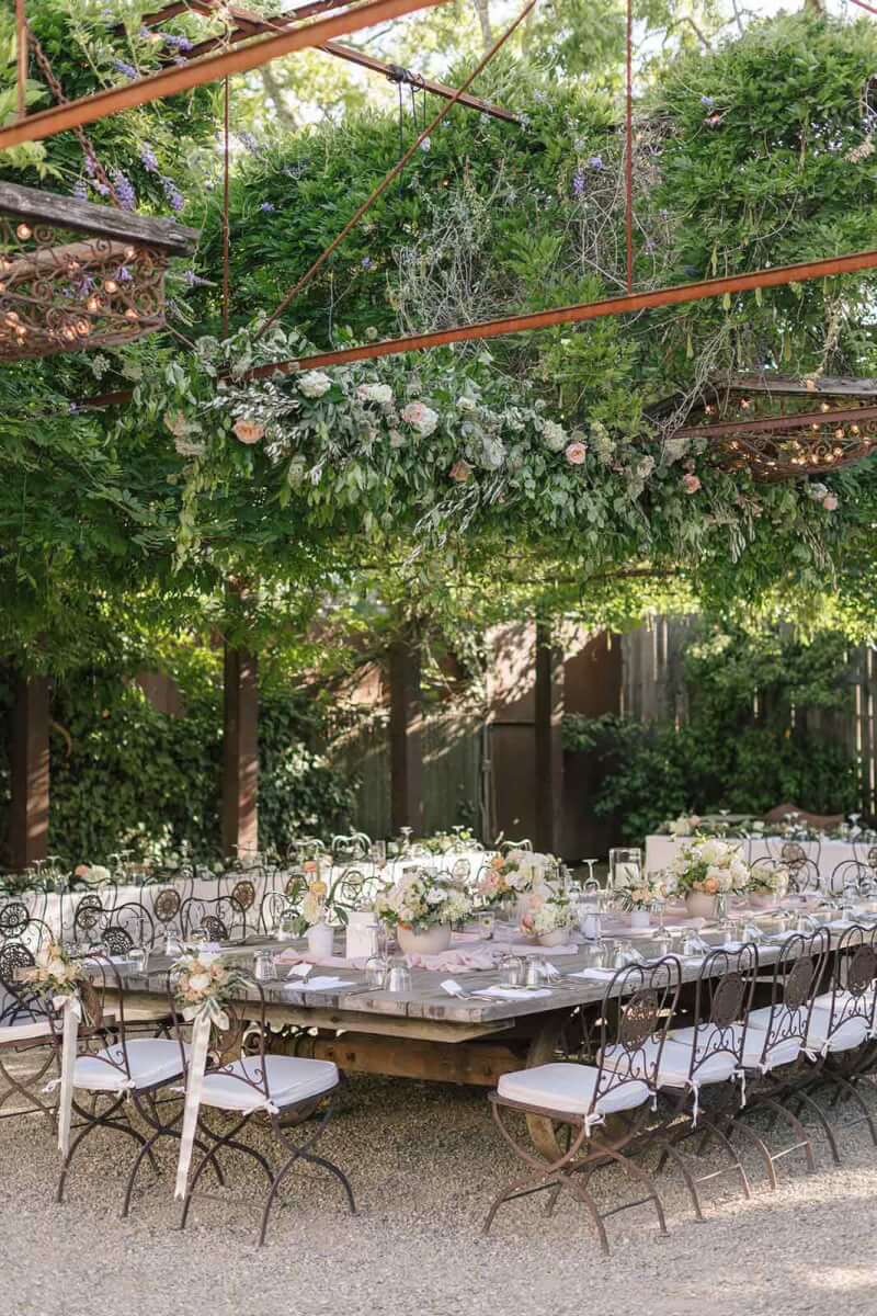 a wedding reception table with floral arrangements, set up for a formal dinner under trellis with hanging flowers