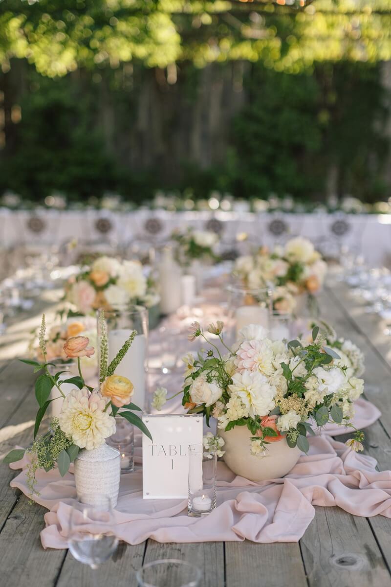 a wooden wedding table topped with white vases filled with gorgeous flowers by Aimee Lomeli designs