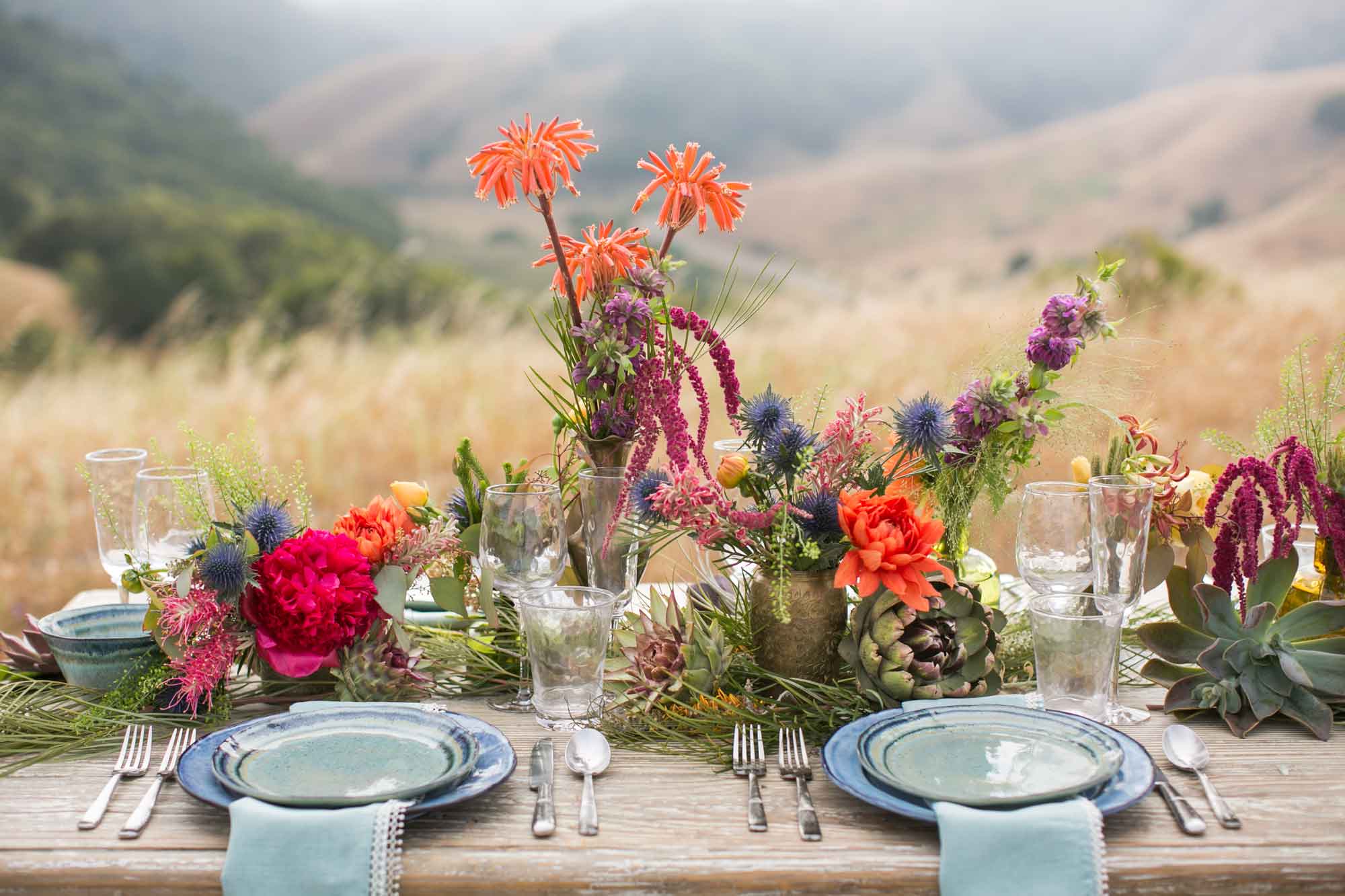 a wooden table topped with plates and vases filled with flowers for a wine country corporate dinner