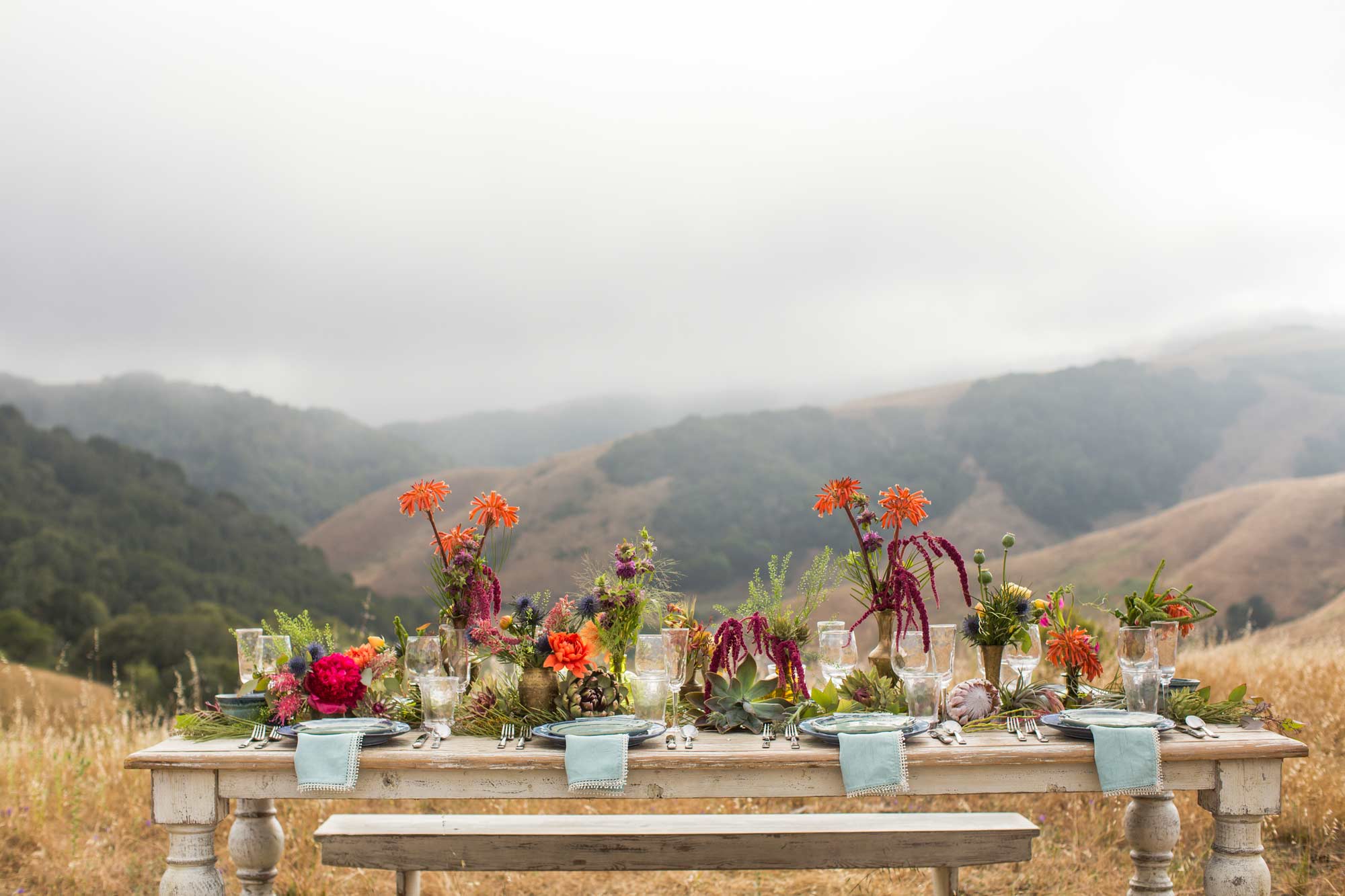 an outdoor table set with abundant colorful flowers with wine country hills in the background