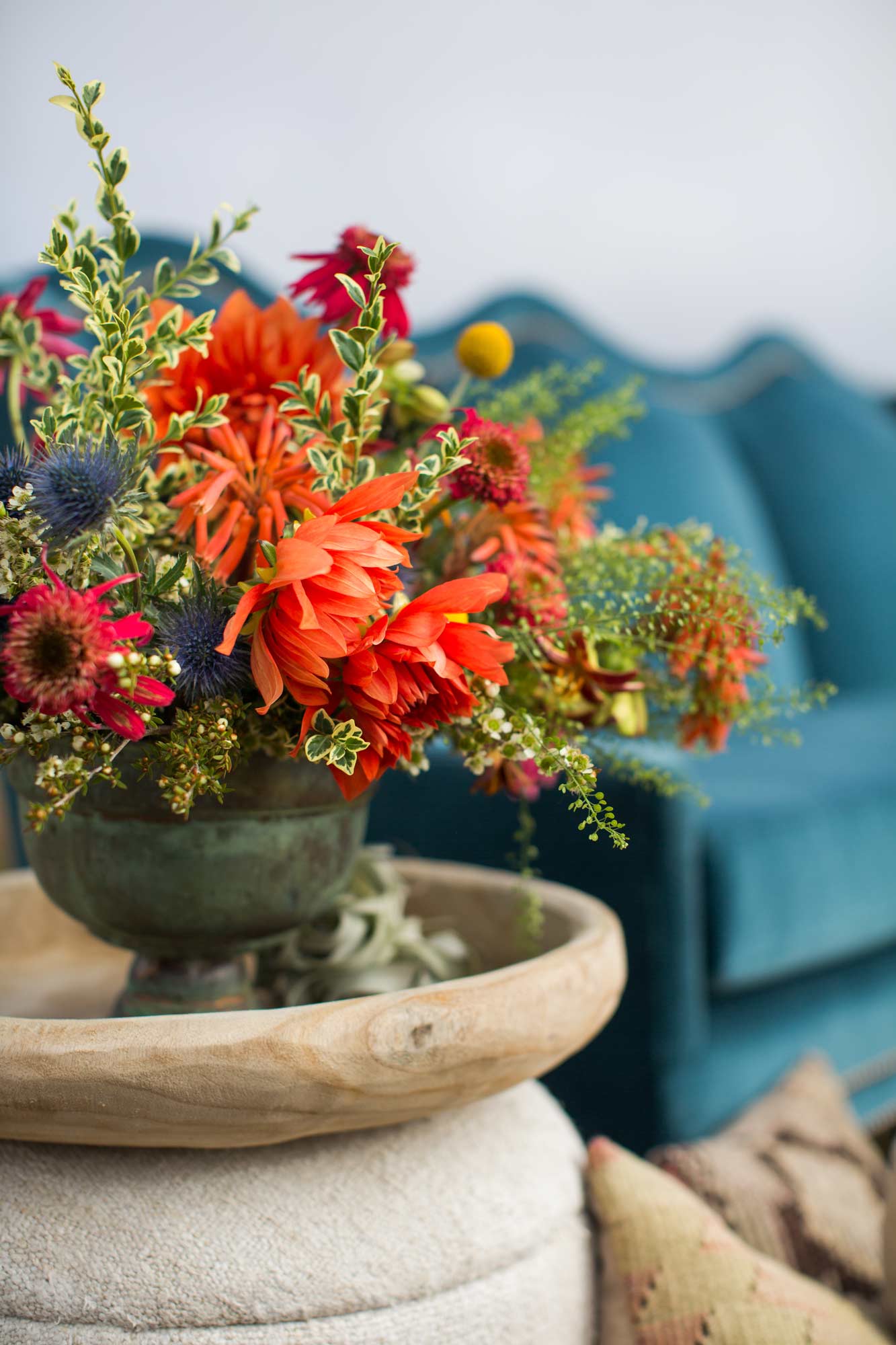 colorful floral arrangement on a wooden tray and boucle ottoman with a blue couch in the background