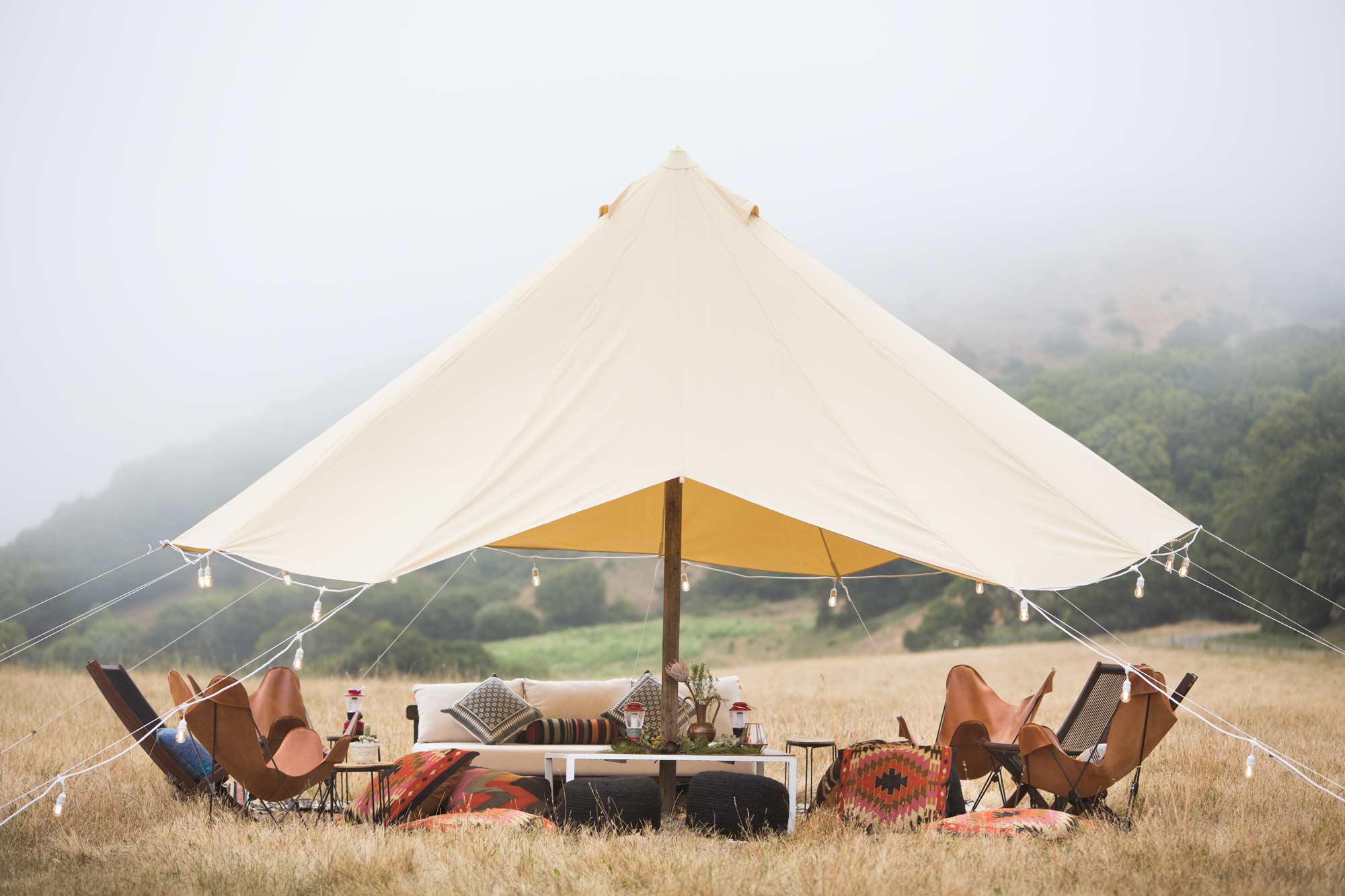 a wine country ranch event tent with chairs and a table with flowers in a field.