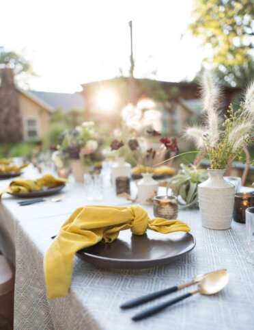 the reflected setting sun behind a table set with flowers and yellow napkins for a private garden party