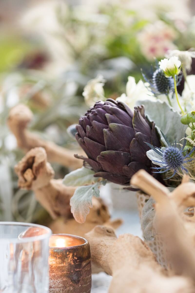a table topped with a vase filled with flowers and a large branch set for a wine country garden party