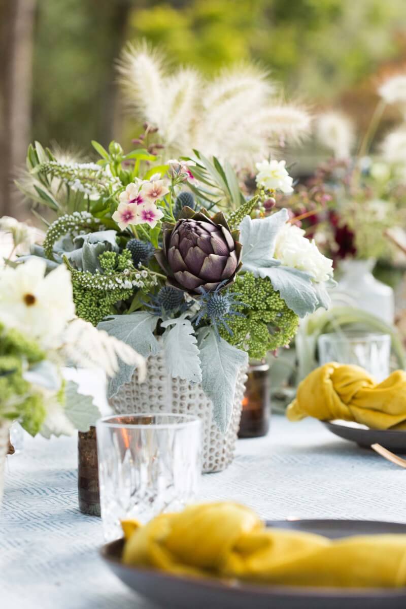 a table set for a wine country garden party topped with vases filled with flowers