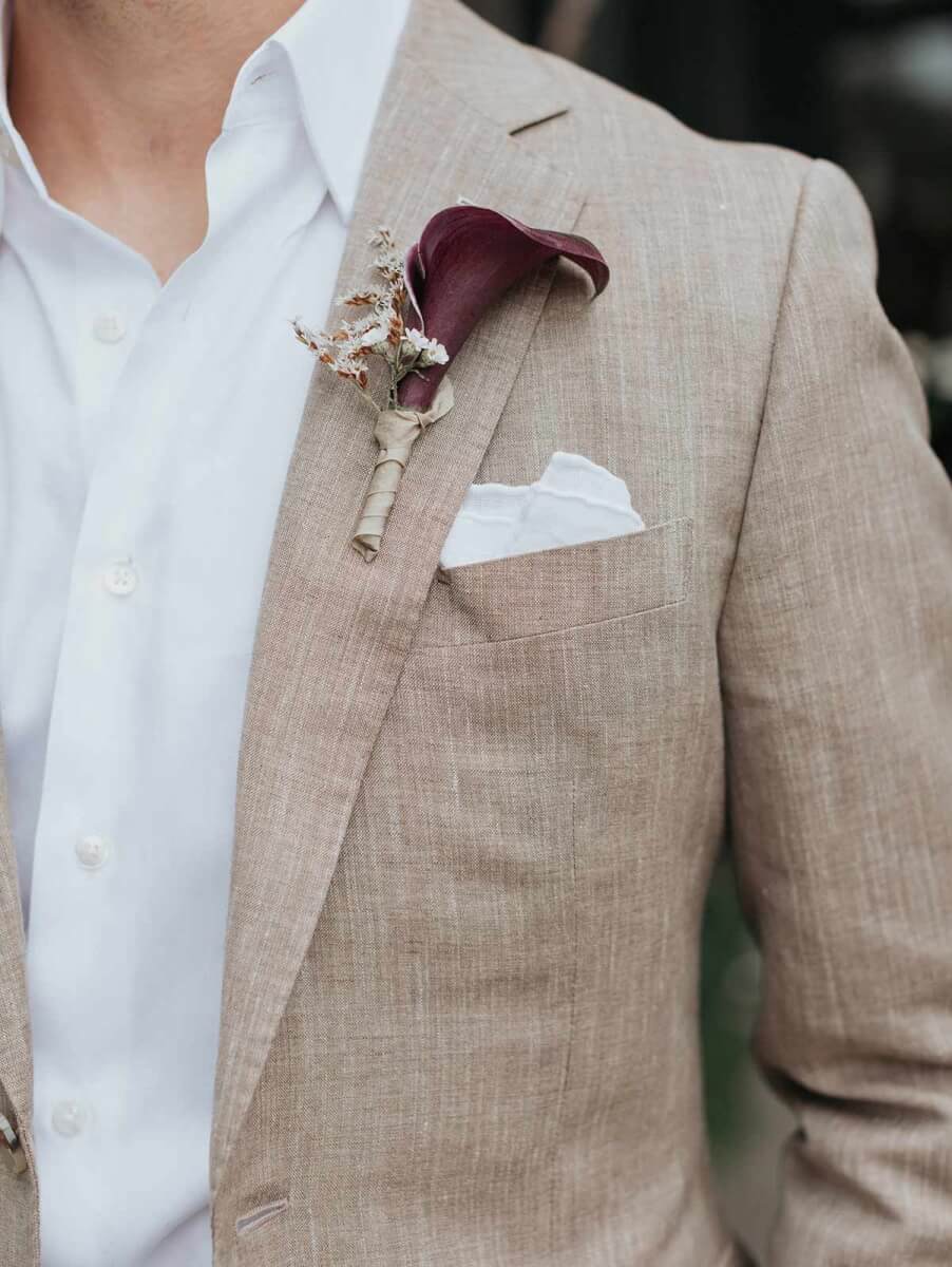 close up of the groom's boutonniere, a plum calla lily with a lacy white floral accent