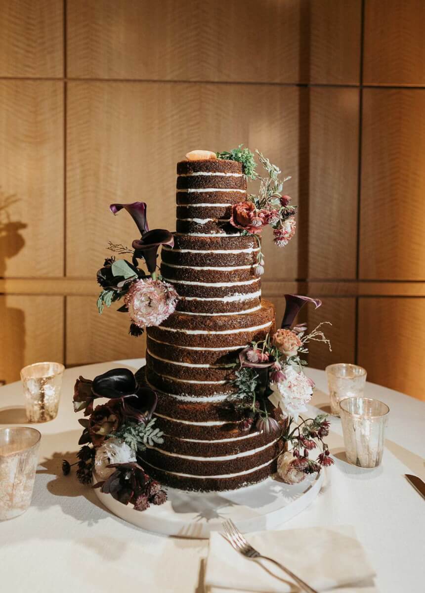 a tall chocolate naked wedding cake adorned with gorgeous flowers