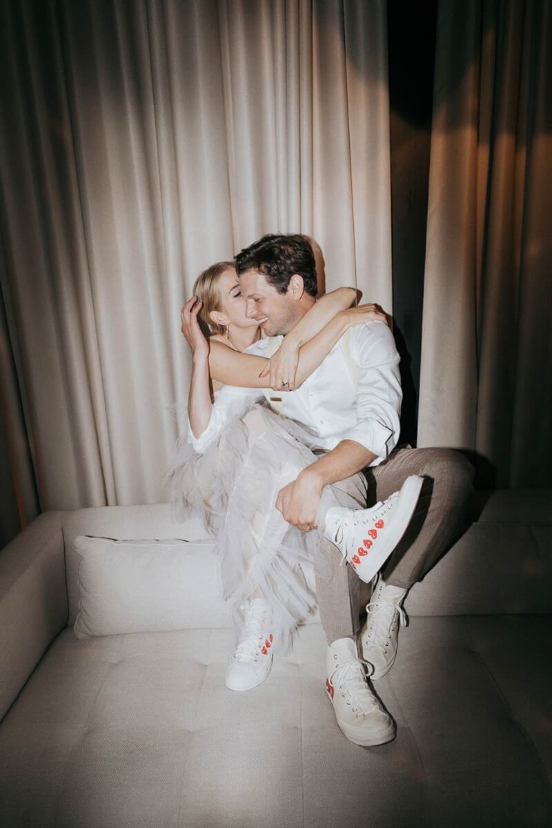 the bride and groom in matching high tops kissing on a couch.